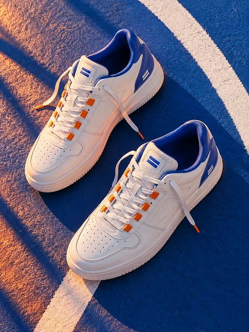 Zwei weiße Sneaker liegen auf einem blauen Basketballplatz entlang einer weißen Linie. Lange Schatten geben dem Foto Tiefe.