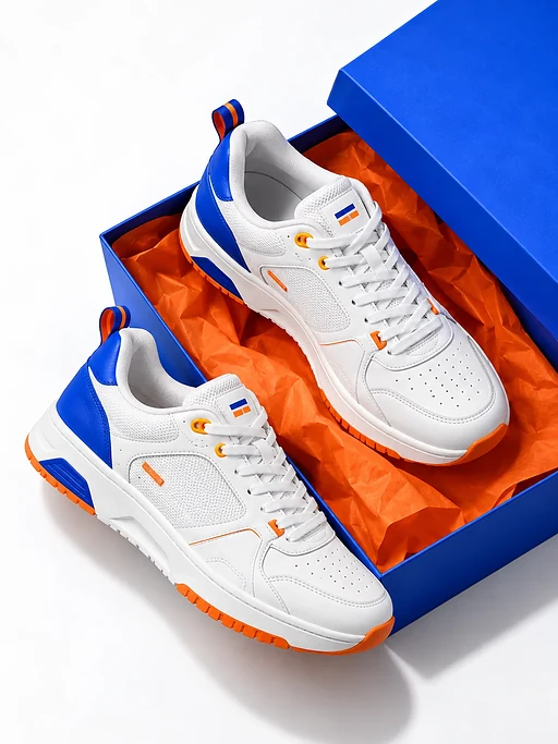 Zwei weiße Sneaker liegen auf einem offenen blauen Schuhkarton mit orangefarbenem Seidenpapier auf weißem Untergrund.